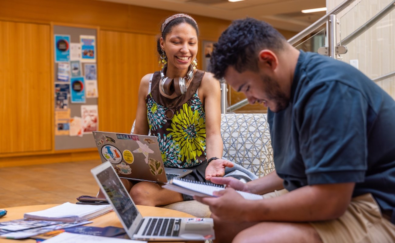 Two students engaged with laptops open, smiling