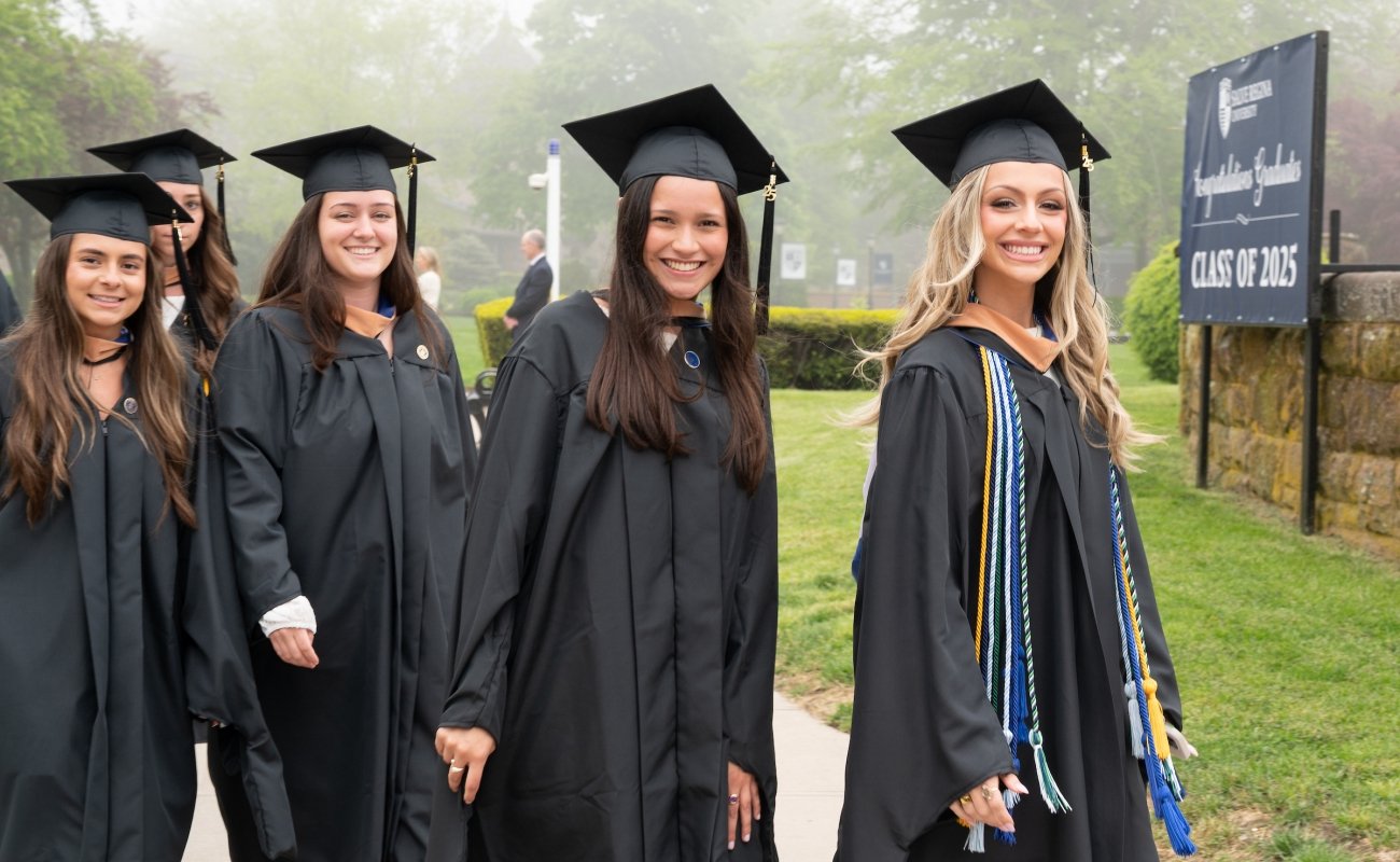 Graduate students dressed in regalia smiling at the camera
