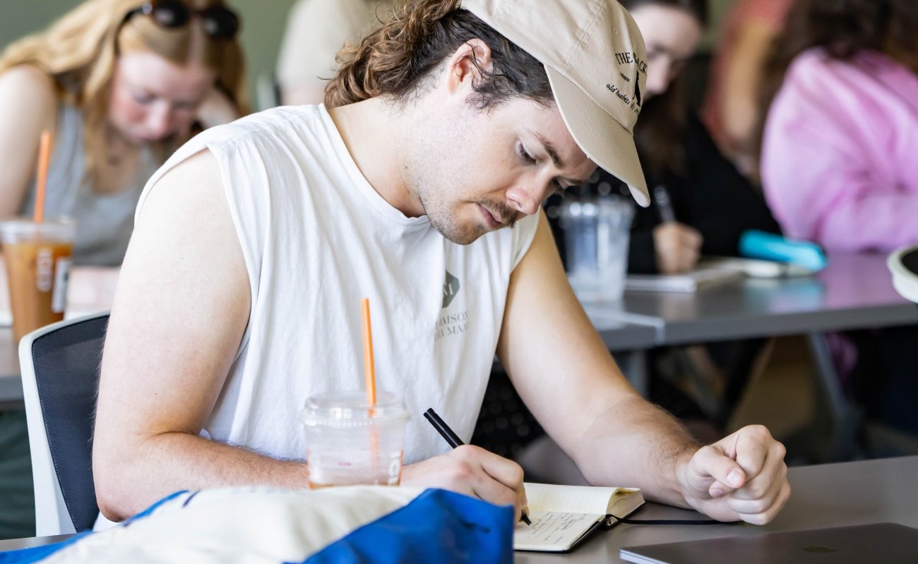 MFA student sitting in class writing in a notebook.