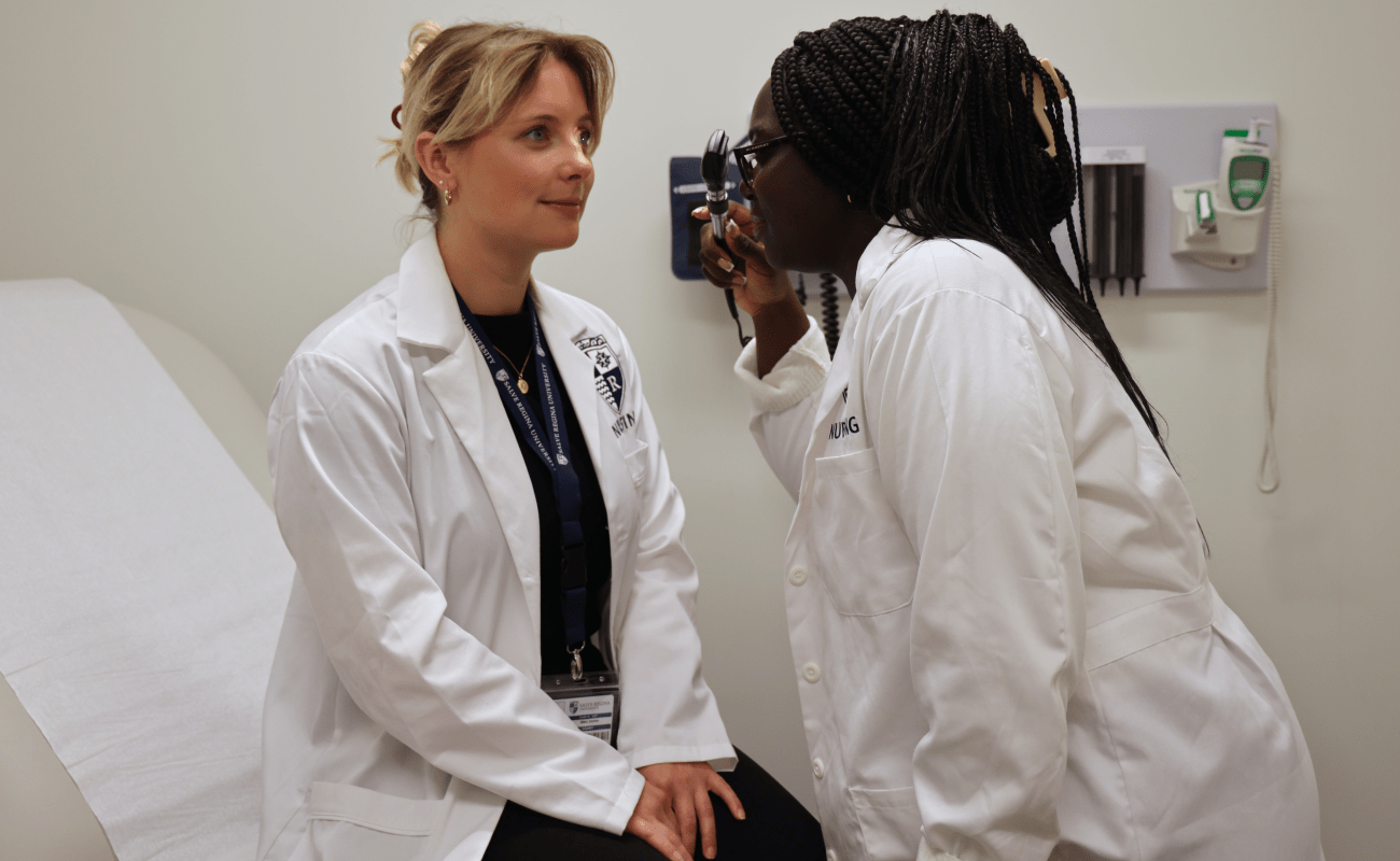 Two graduate nursing students practice using an ophthalmoscope on each other.