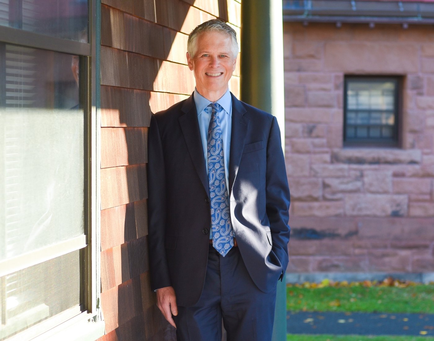 Program director leaning against shingled building smiling at camera