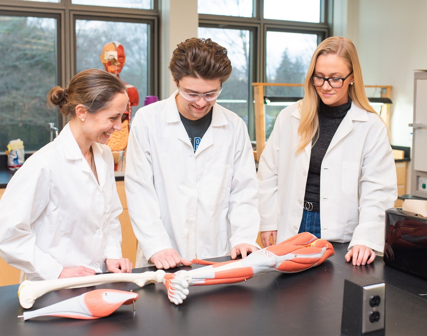 two students and professor study leg model