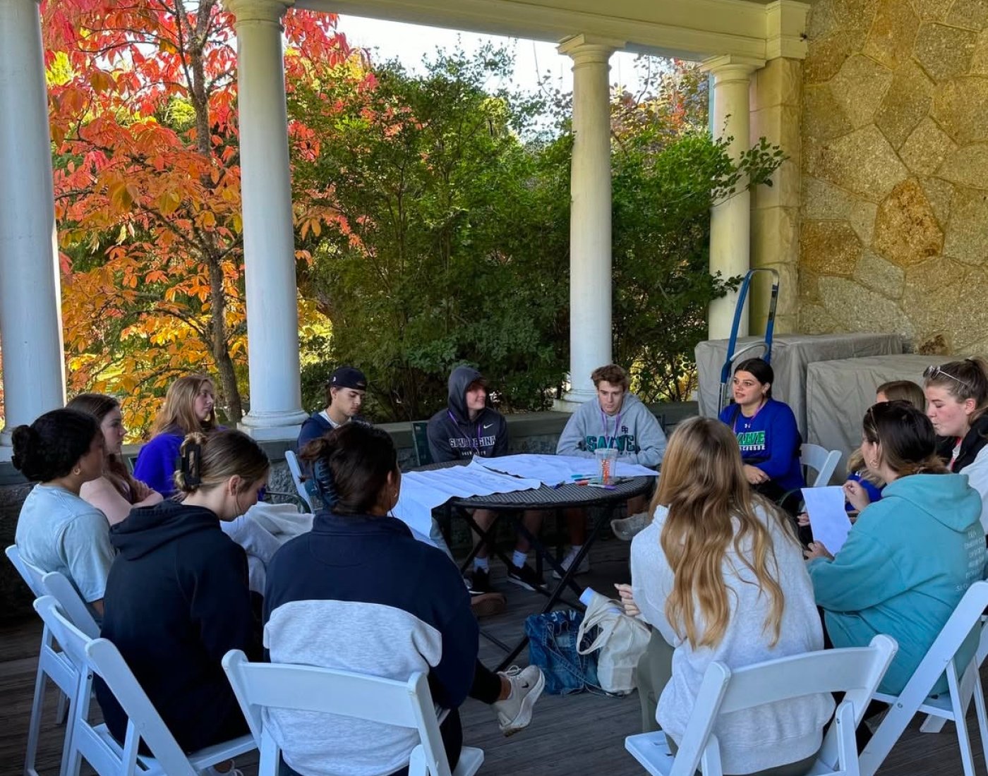 Students build relationships around a table in a beautiful location with a colorful tree