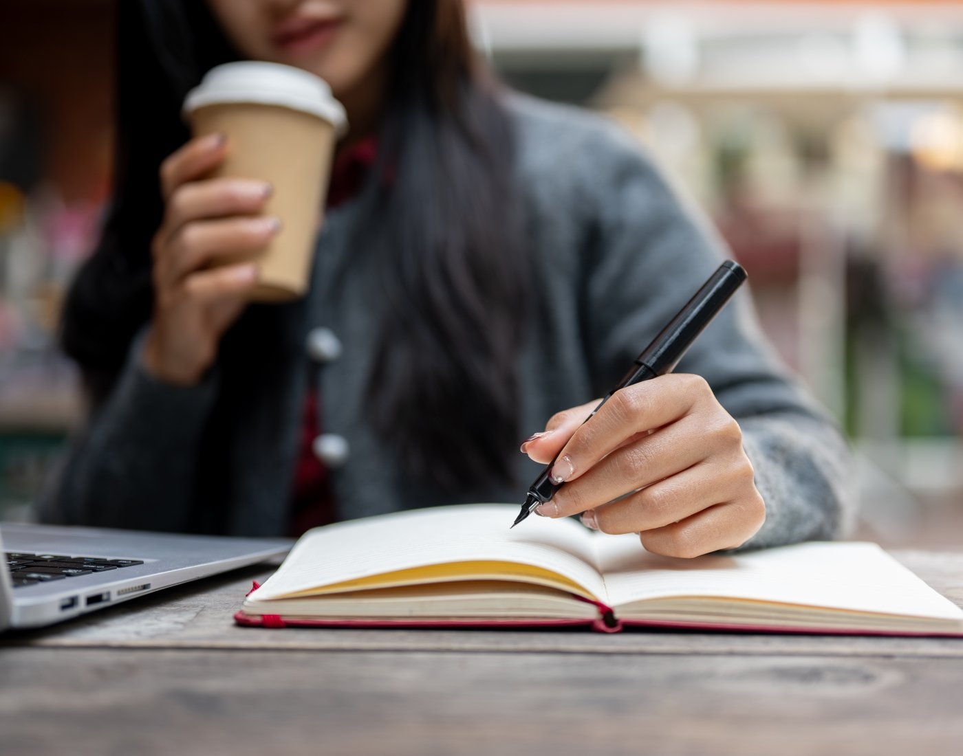 Girl sipping a coffee in cafe while she writes in a notebook.