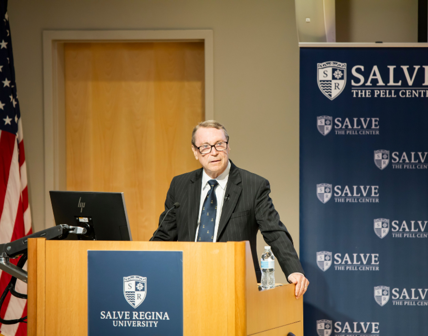 Craig Symonds standing at a podium giving his McGinty Lecture, with Salve branding and an American flag behind him.