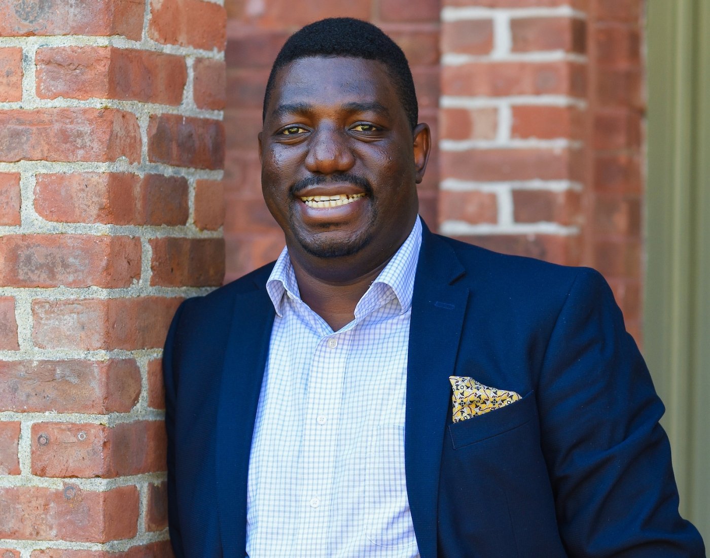 Dr. Yvan Ilunga smiling at the camera leaning against a brick wall.