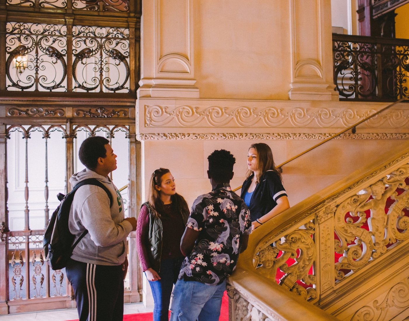Small tour group on stairs inside Ochre Court, next to ornate railing