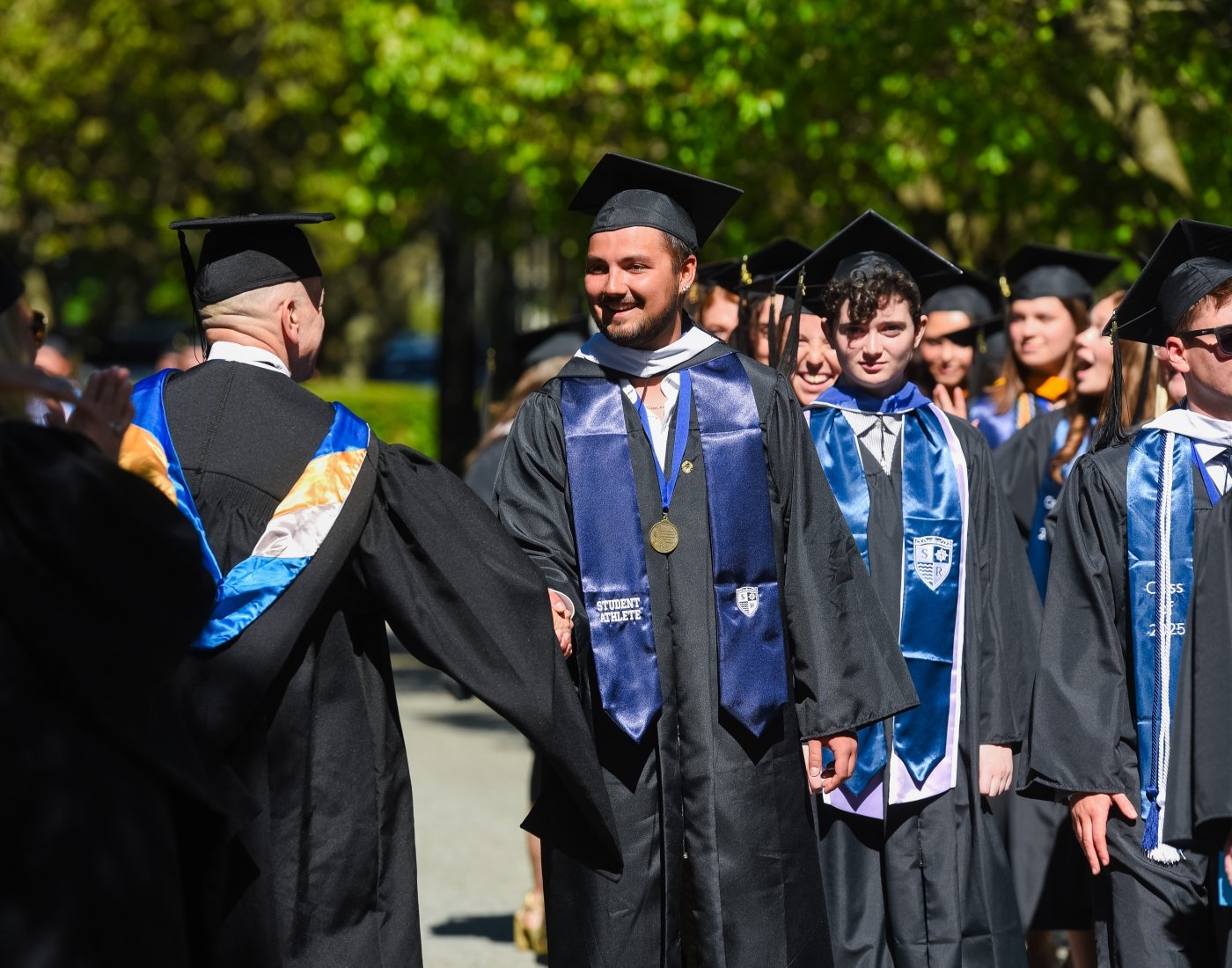 A man in a graduation procession shakes hands with a faculty member.