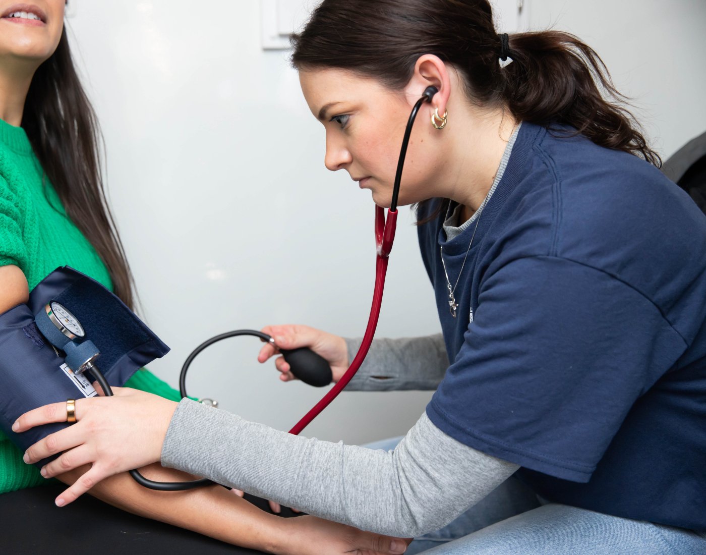 Healthcare worker measuring a seated patient’s blood pressure with a cuff and stethoscope.