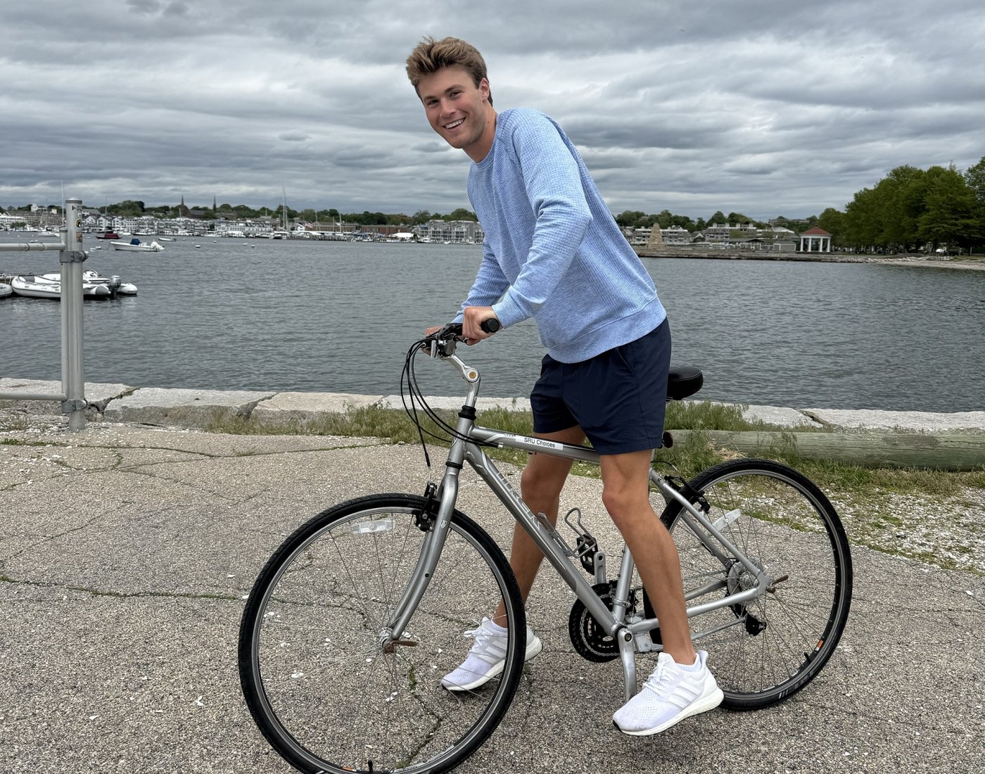 A young man rides a bicycle near the ocean.
