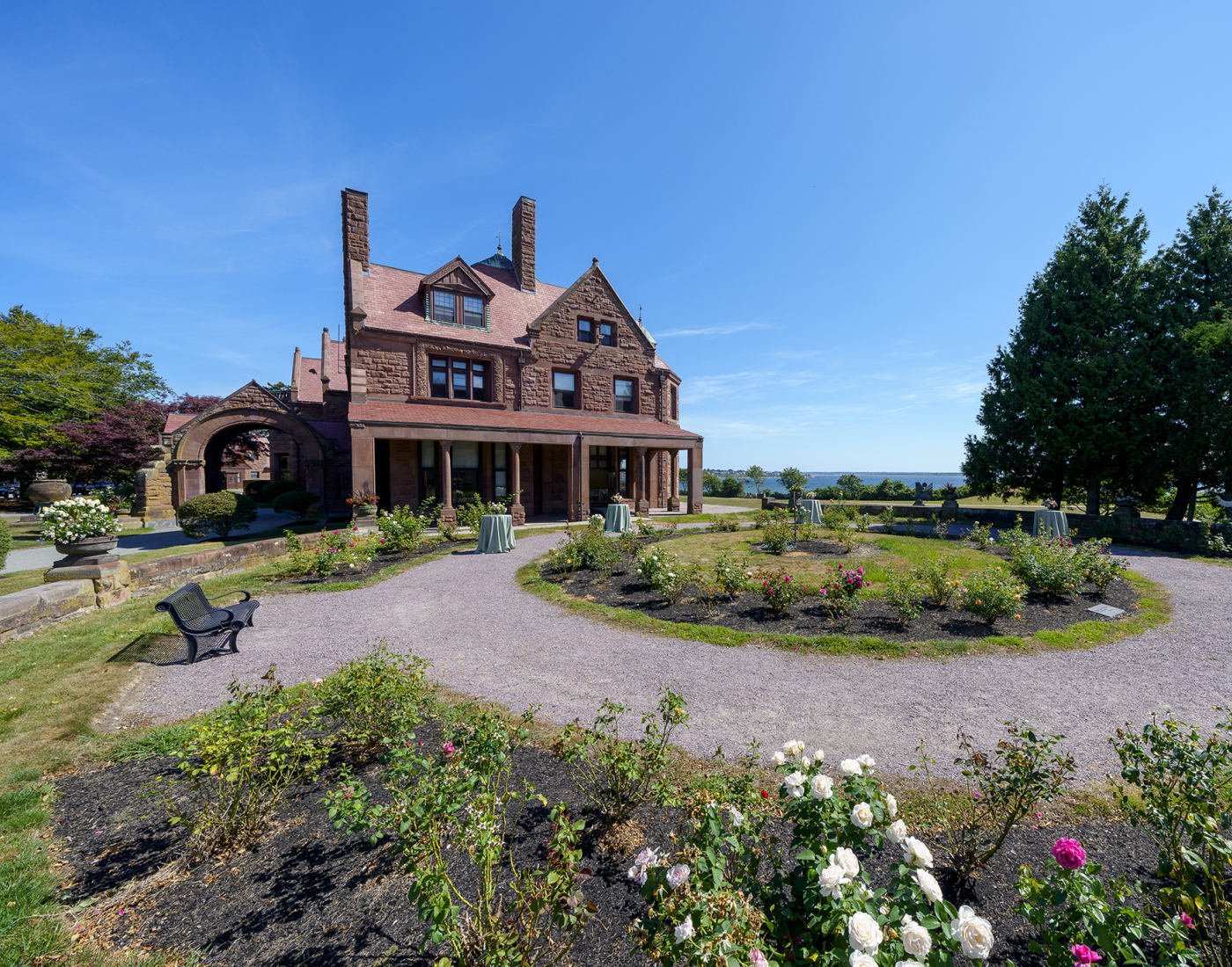 Historic stone house with a covered porch, surrounded by a landscaped garden with walking paths and flowering shrubs.