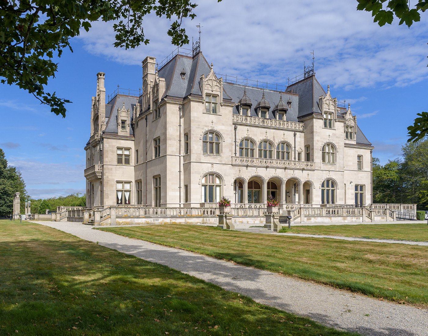 A stone mansion with ornate gables and arched windows, set on landscaped lawns under a blue sky.