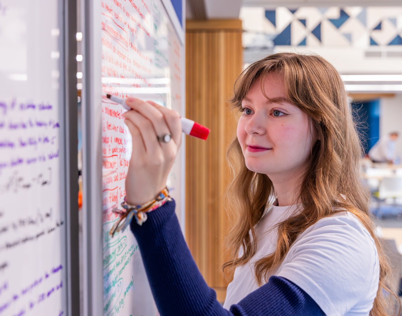 Female student faintly smiling writing equations on a white board.