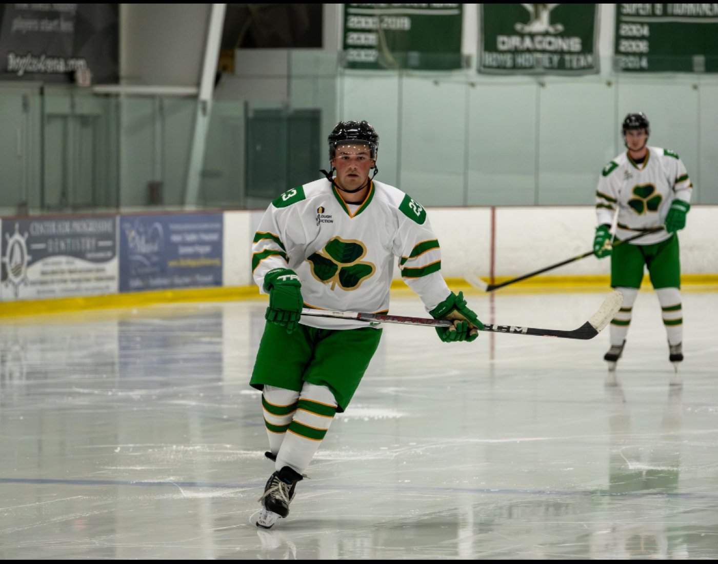 Connolly on the ice rink in his green and white hockey uniform, holding his stick.