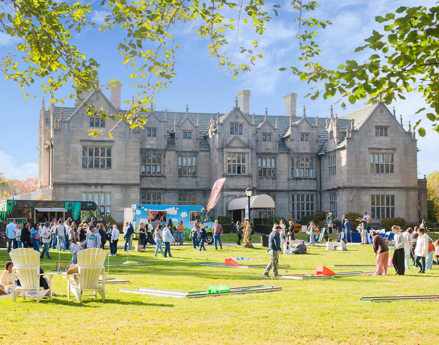 A large group of people gather and play games on a lawn in front of a historic stone mansion.