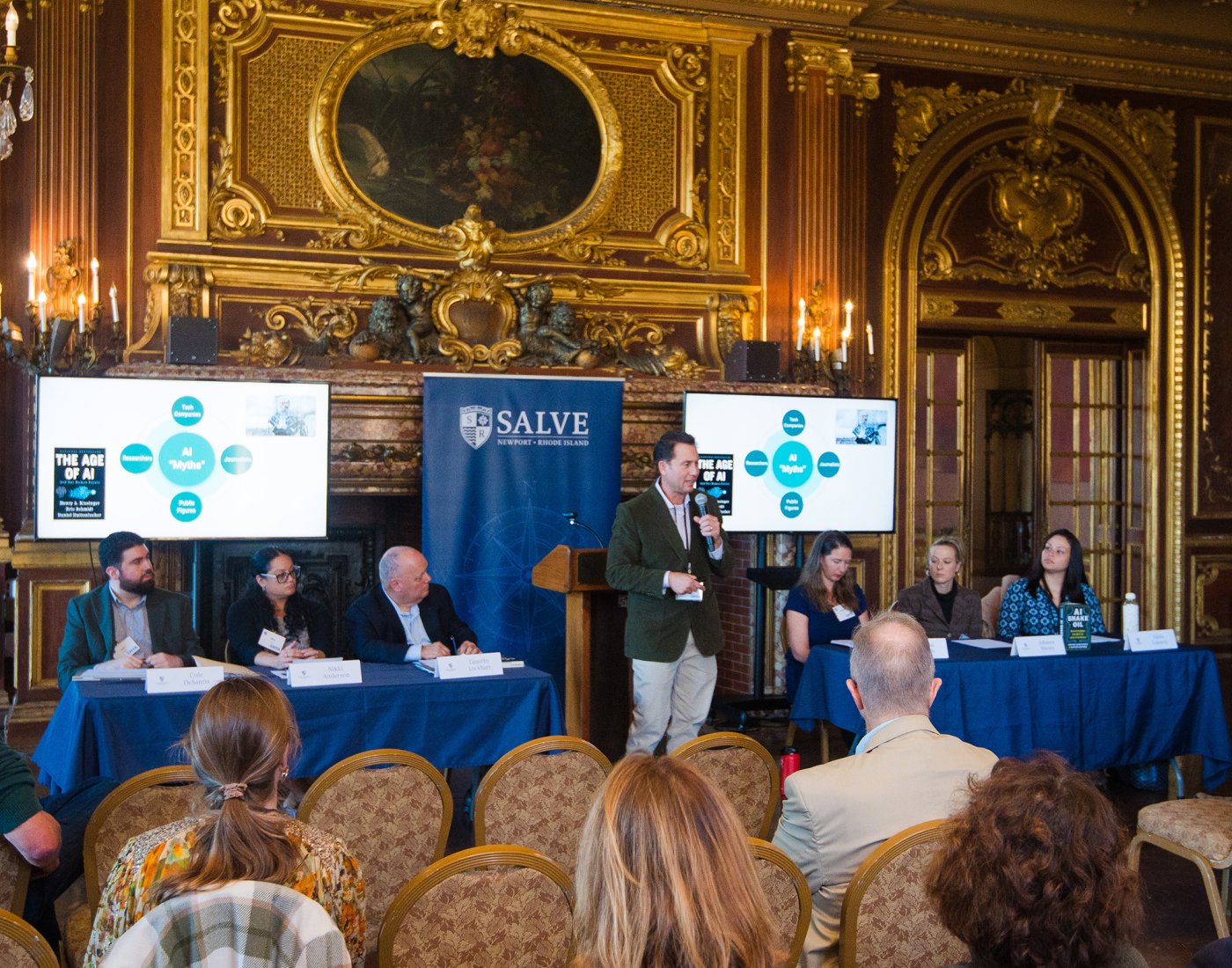 Panel discussion at a conference, with a speaker standing at a podium and seated panelists facing an audience.