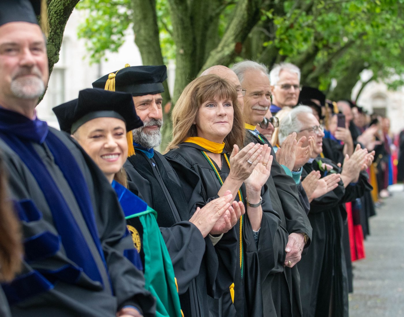 faculty in their regalia clapping as students walk down to graduation.