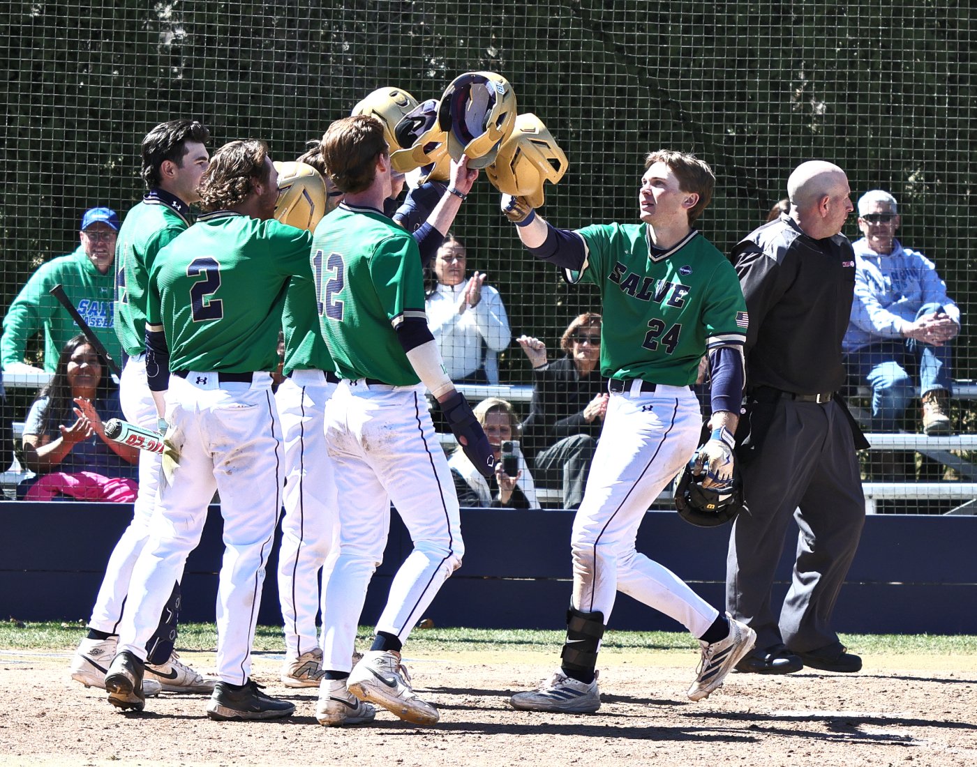 Baseball players in green jerseys bumping their helmets together in their hands.