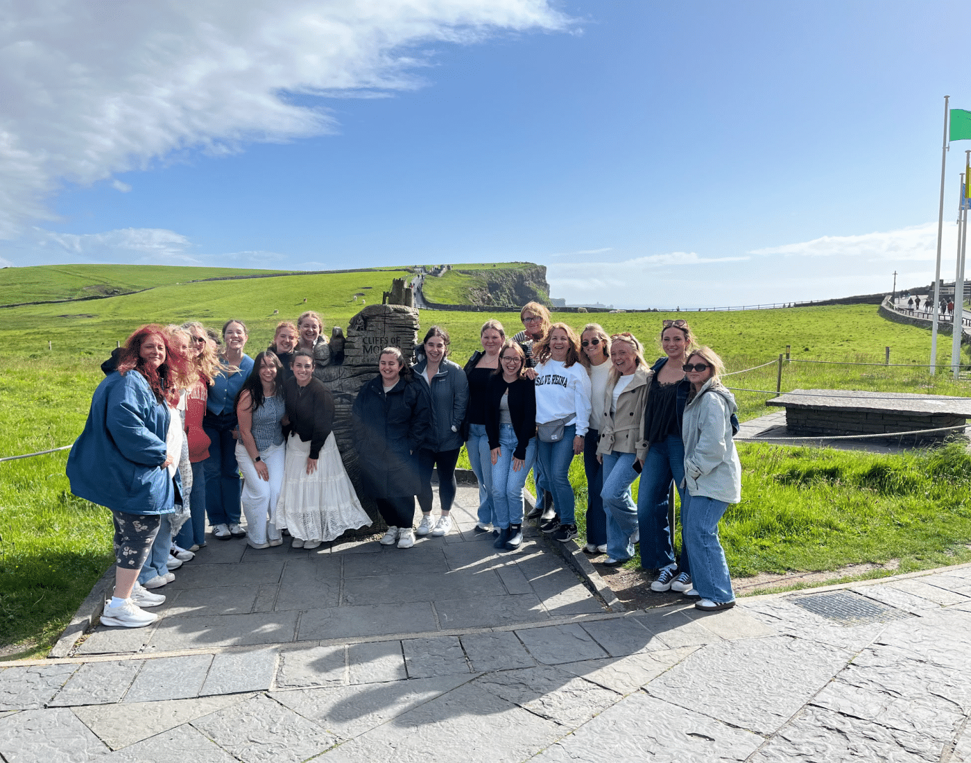 female students and faculty smile for a group photo in Ireland in front of a field of grass.