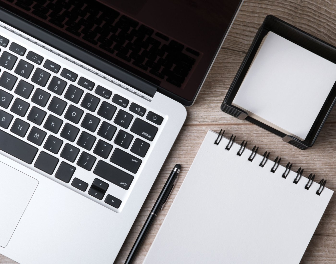 An open laptop computer next to a blank notebook, pen and sticky notes.