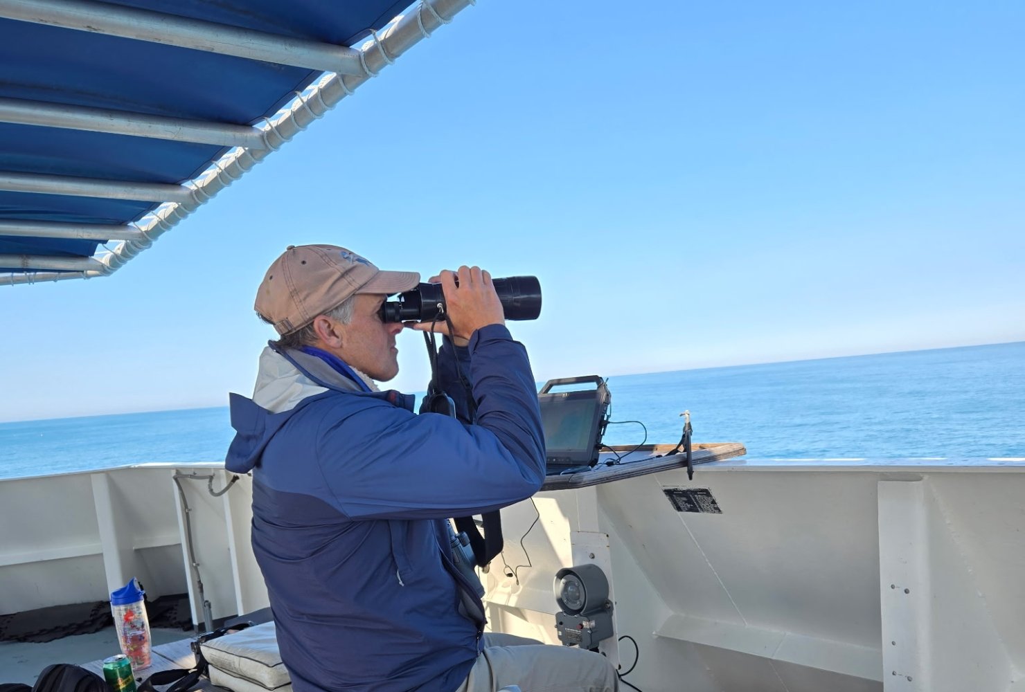 Chace on a boat looking out into the water with binoculars.