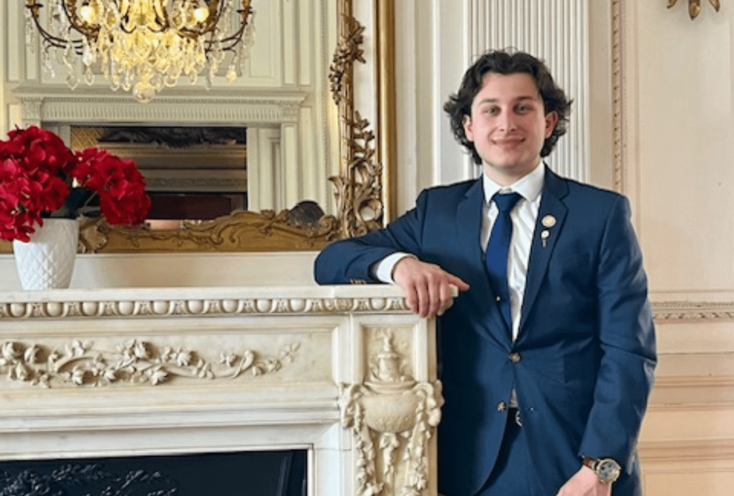 Photo of Silva in a suit smiling and leaning against a white fireplace mantle.
