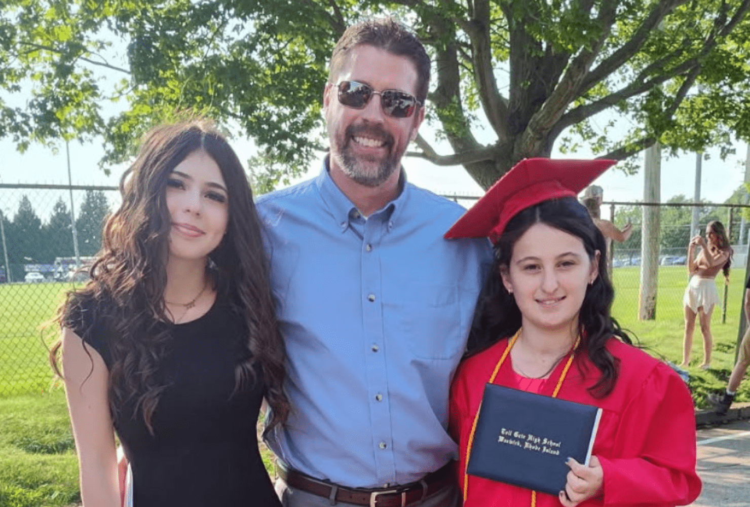 Corey smiling next to his daughters at a high school graduation.