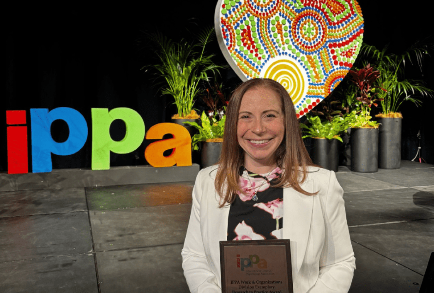 Perry smiling holding her iPPa award in front of a rainbow IPPa sign.