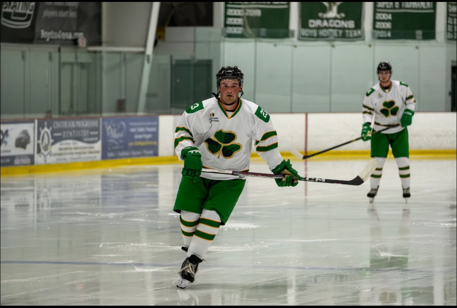 Connolly on the ice rink in his green and white hockey uniform, holding his stick.
