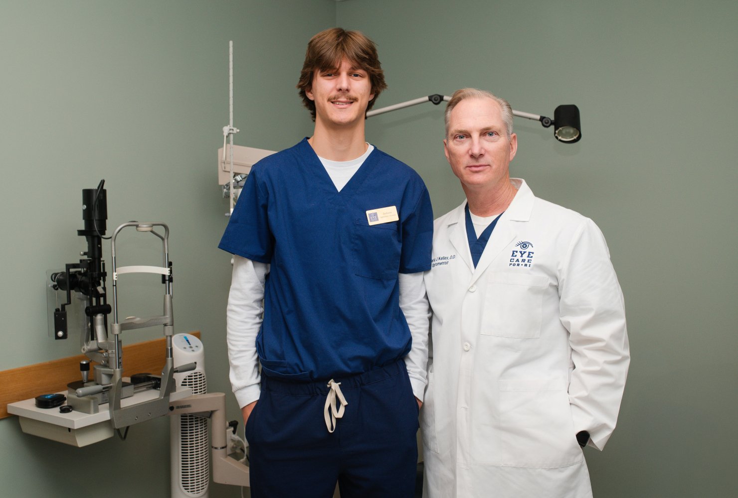 Optometrist and intern standing in eye exam room posing for photo.