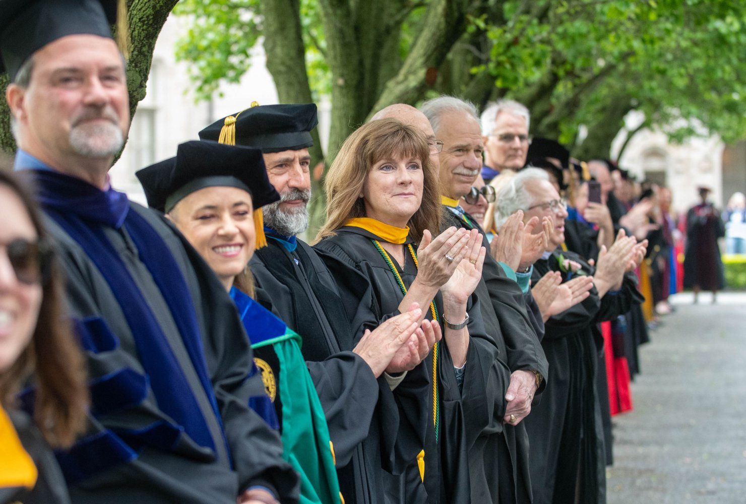 faculty in their regalia clapping as students walk down to graduation.