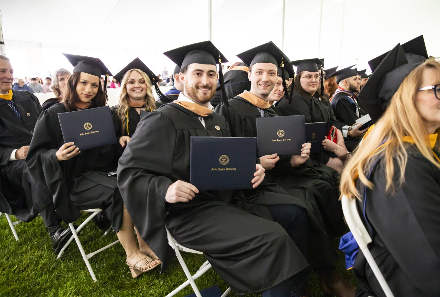 Students at the Commencement ceremony sitting and smiling in their regalia with their diplomas in hand.