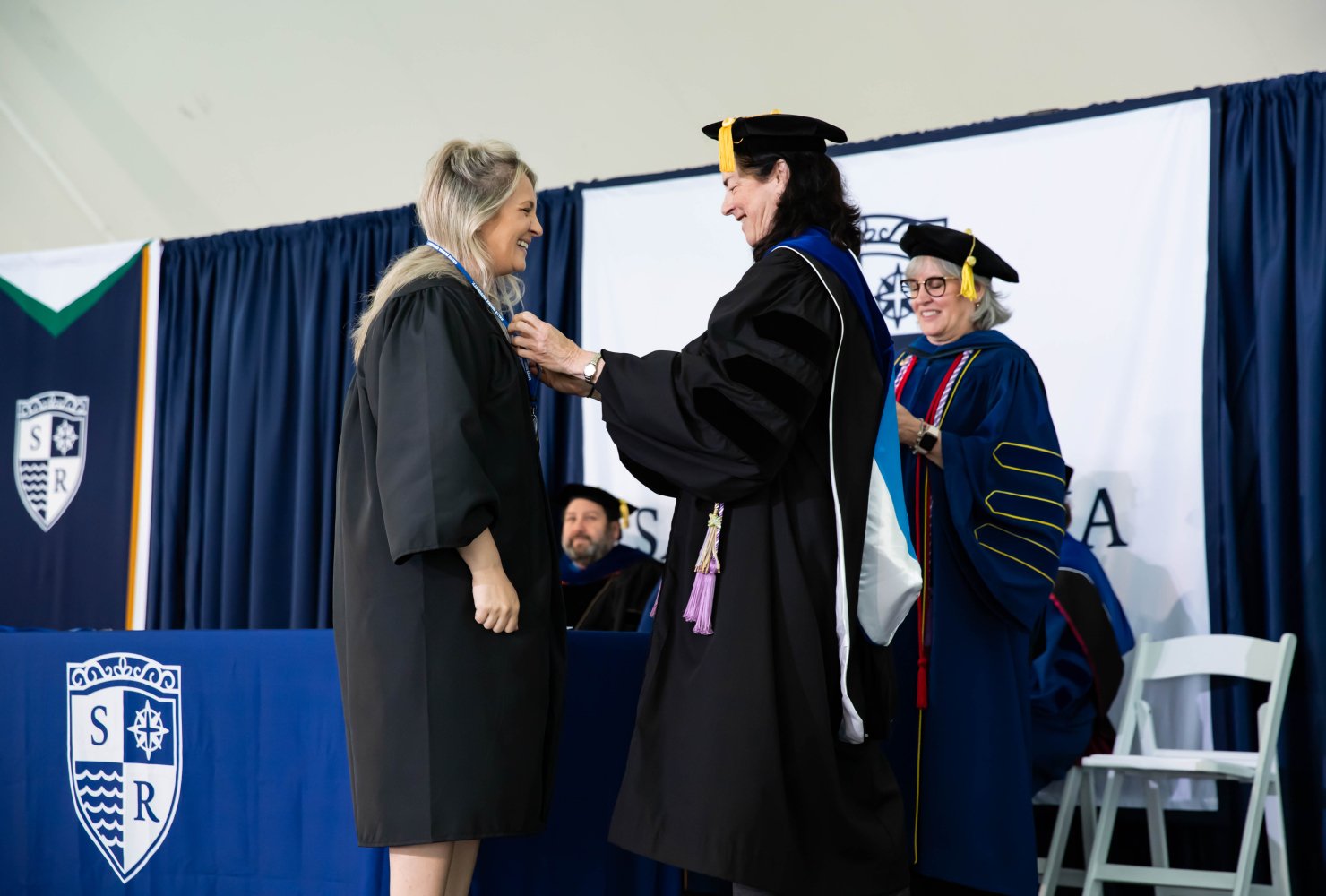 Student and faculty in black robes at nursing pinning ceremony