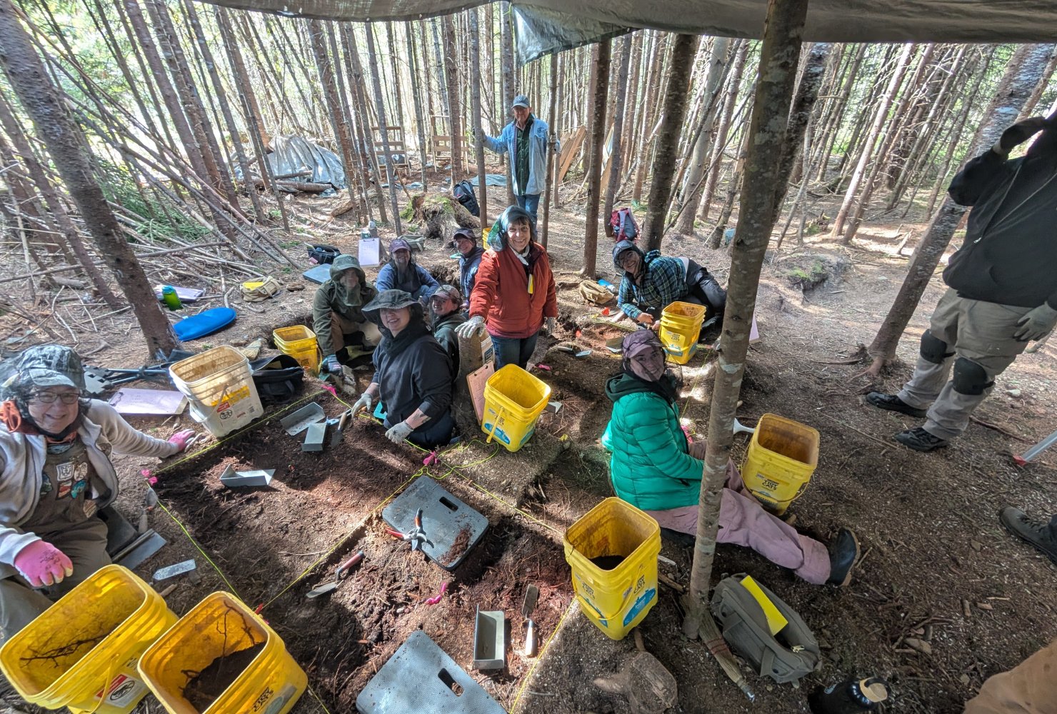Students smiling in their test pits during an excavation in the woods.