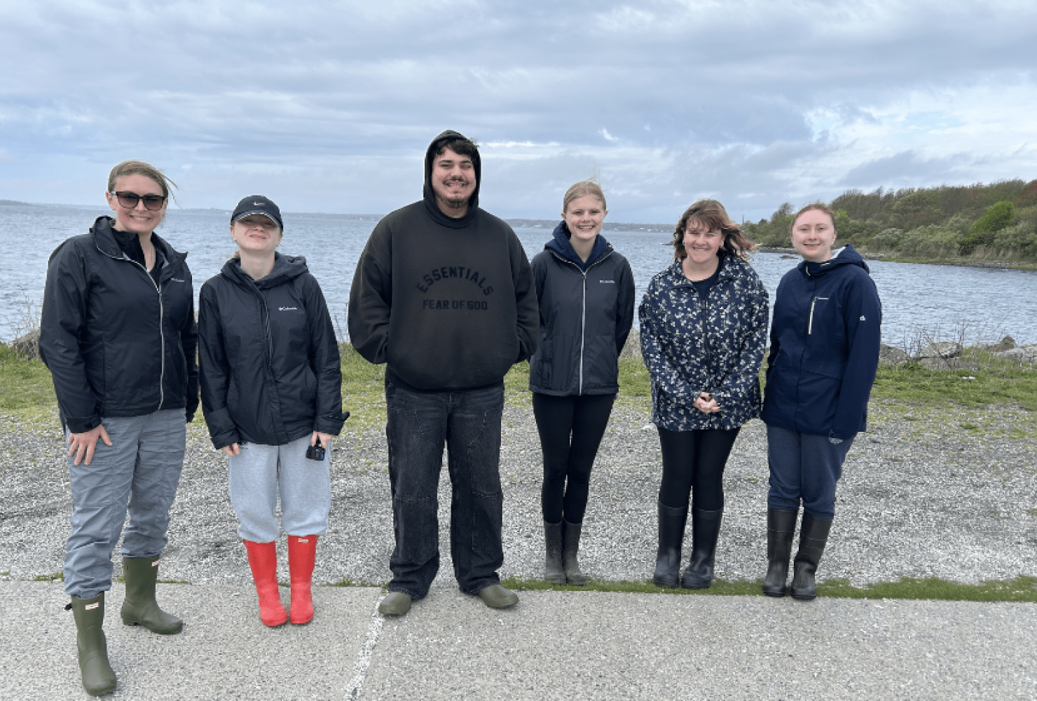 group photo of six people outside in front of the ocean.