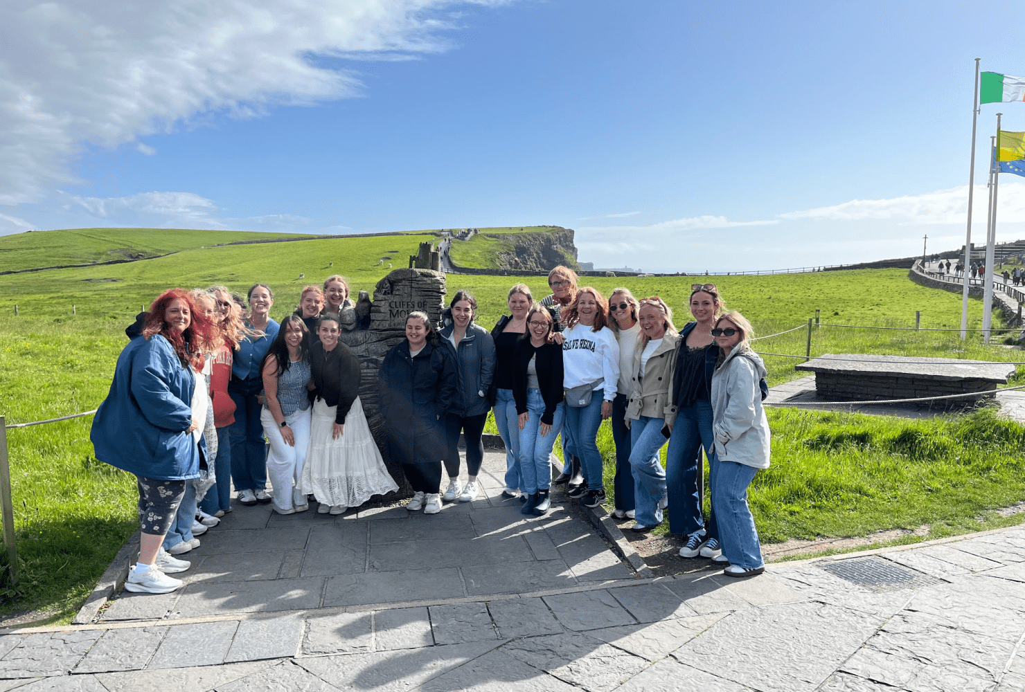 female students and faculty smile for a group photo in Ireland in front of a field of grass.
