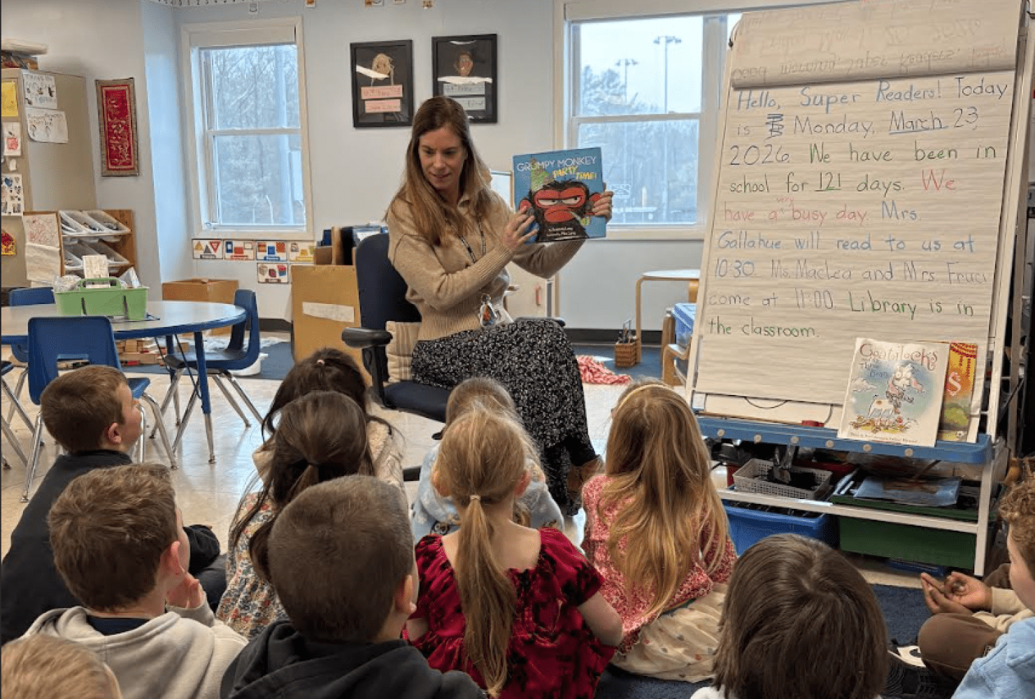 Teacher reads a picture book to students seated on a classroom rug.