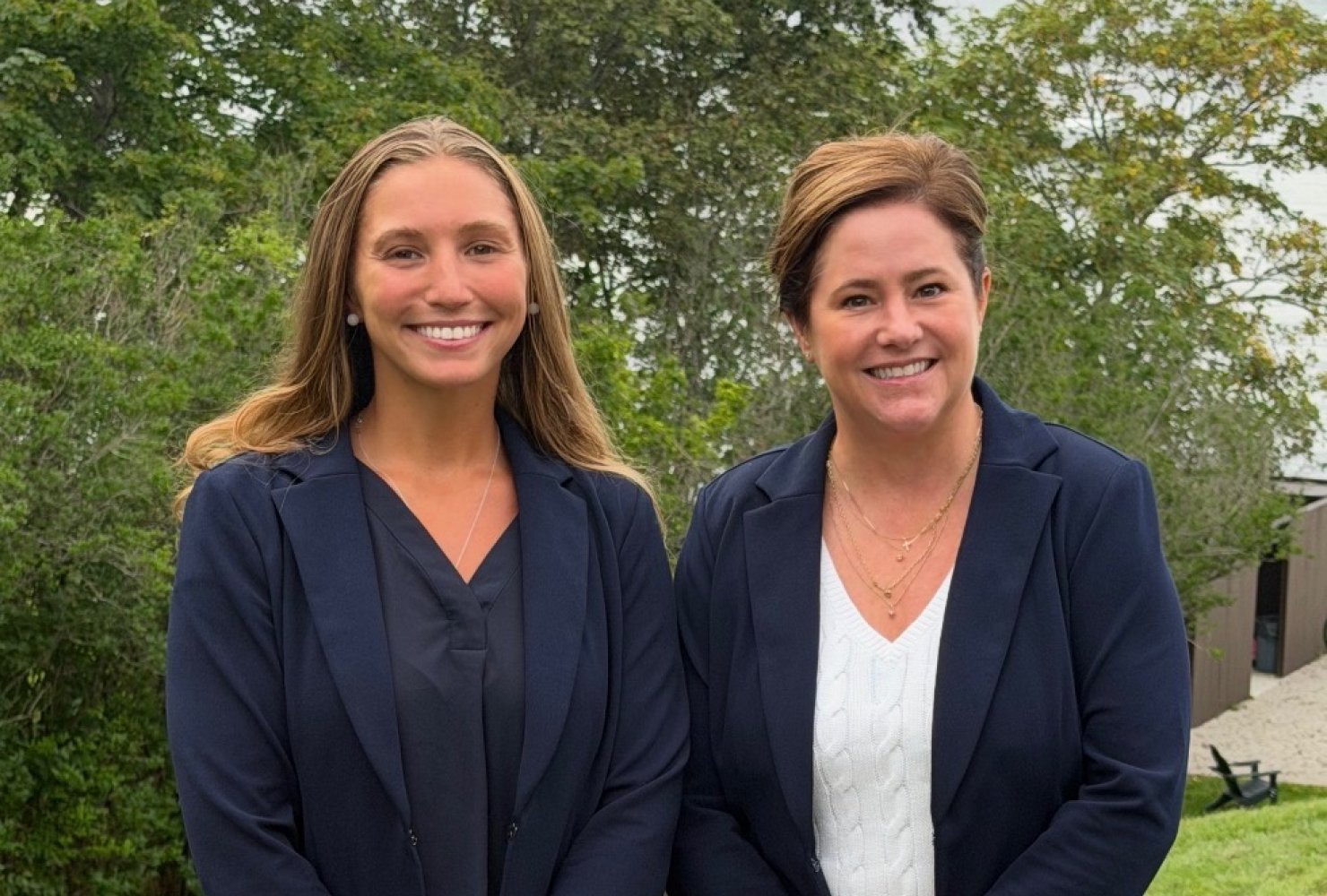 Two women stand together outdoors with Newport Harbor in the background.