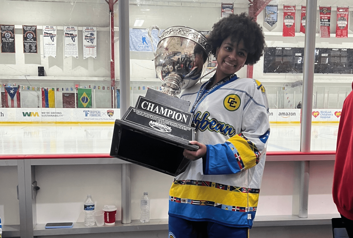 Aryana in hockey jersey holding large trophy.