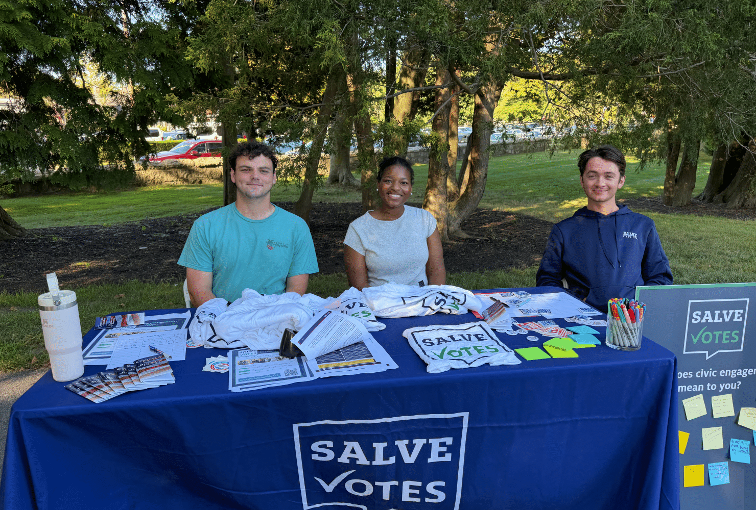 Three SalveVotes student members sit behind a voter engagement table outdoors on campus.