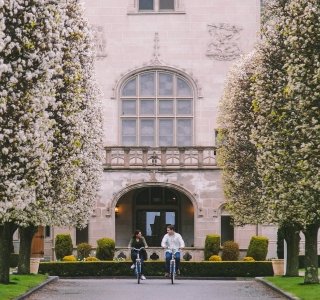 Front of Ochre Court with two students riding bikes