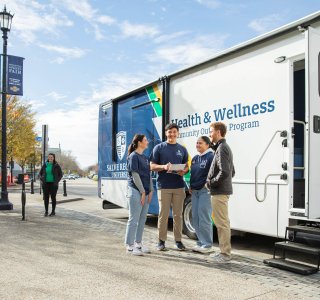 A group of four young adults stand and talk beside a mobile vehicle