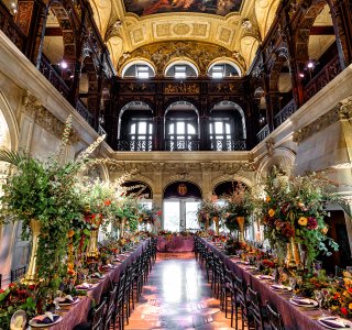 A three-story great hall with an intricately painted ceiling, set with long tables.