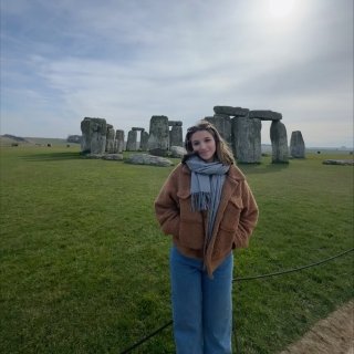 Defelice is smiling, bundled up in front of Stonehenge, a prehistoric megalithic structure in Wiltshire, England.