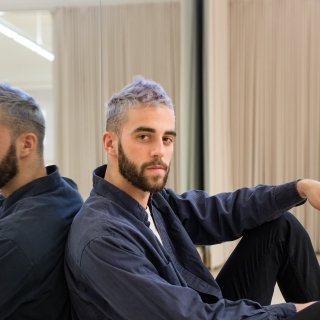 Young bearded man with short purple hair leaning against a mirror