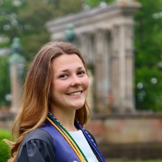 Brunette long hair graduate in gown holding cap, smiling on commencement day