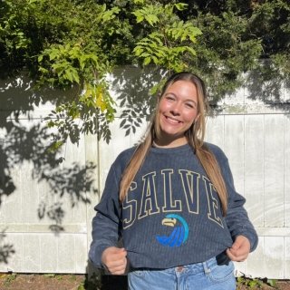 female student outside surrounding by green foliage in salve sweatshirt