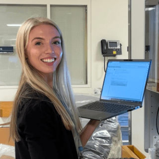 Cara working at the hospital smiling toward camera holding a computer.