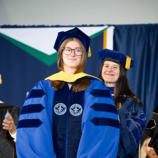 Behavior Analysis Ph.D. graduate Hannah Grey on stage at commencement in full doctoral regalia 
