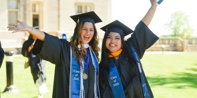 Two female students celebrating at graduation outside Ochre Court on a sunny day